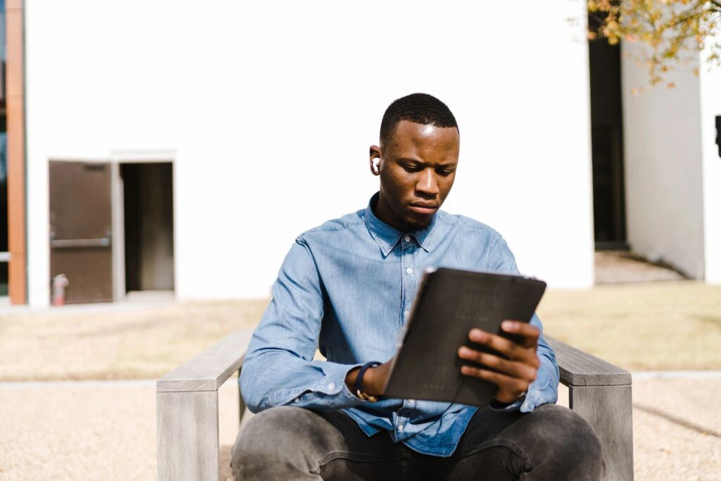 A man sitting on top of a bench looking at an ipad.